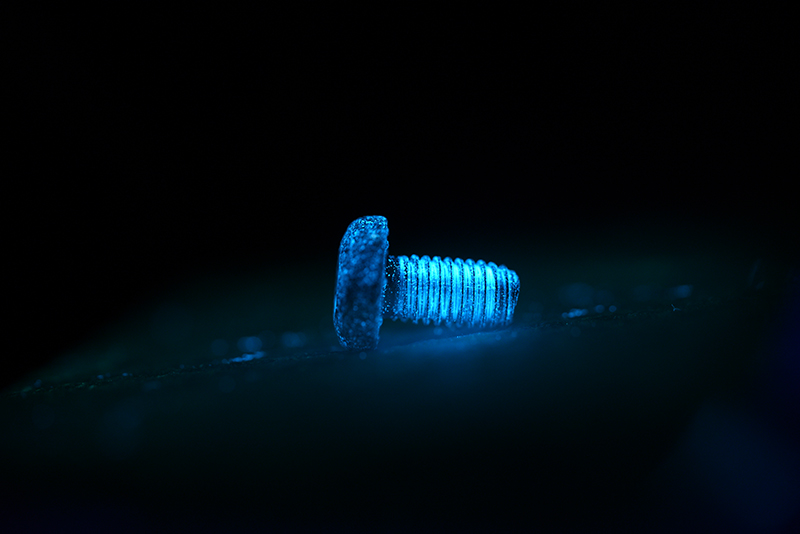 Een schroef onder UV-licht. De vele witte puntjes zijn stofdeeltjes.